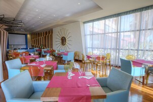 Un restaurante con varias mesas y sillas, un espejo grande y vistas al exterior.