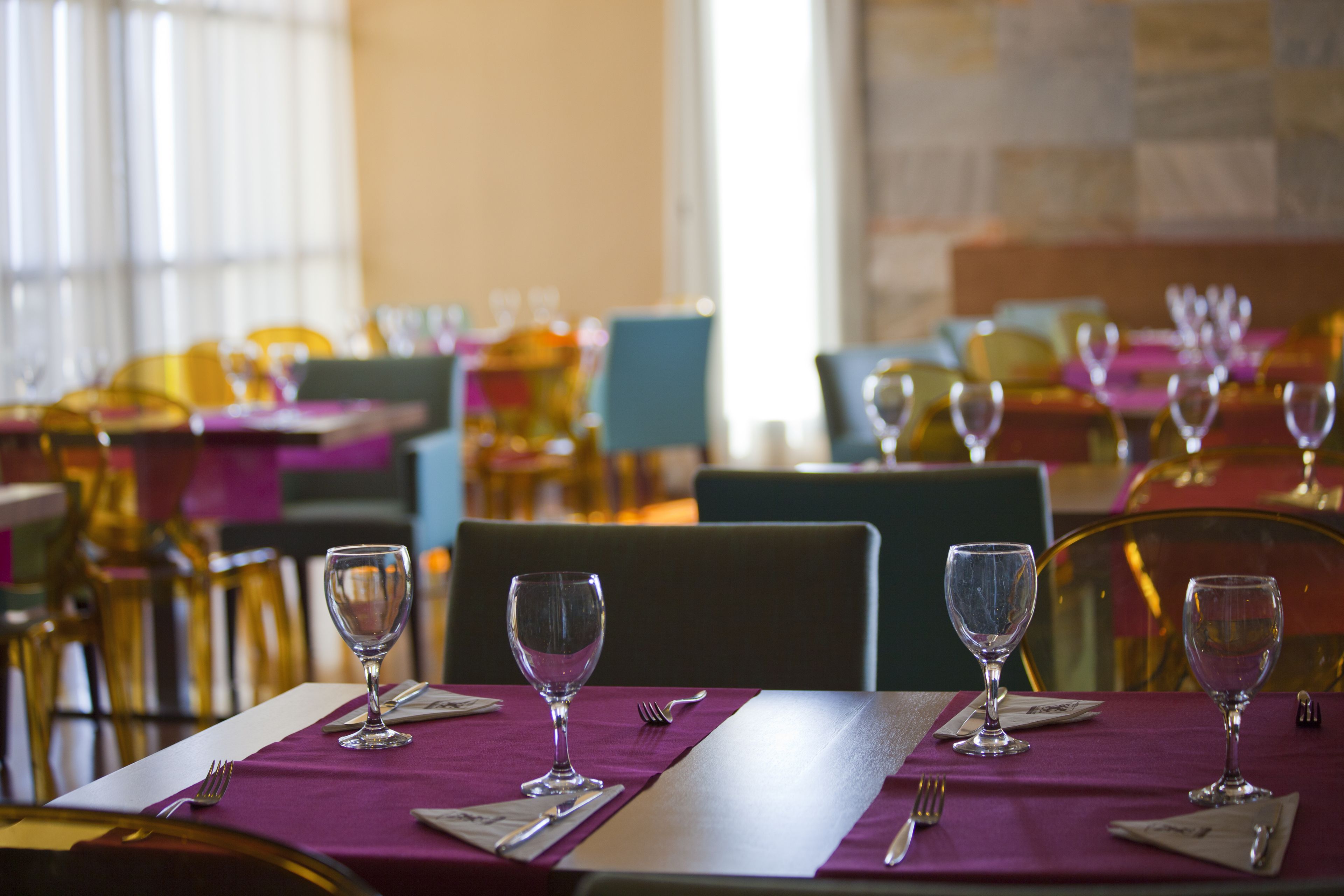 A dining area with tables set for two, each with a wine glass, cutlery, and napkins.
