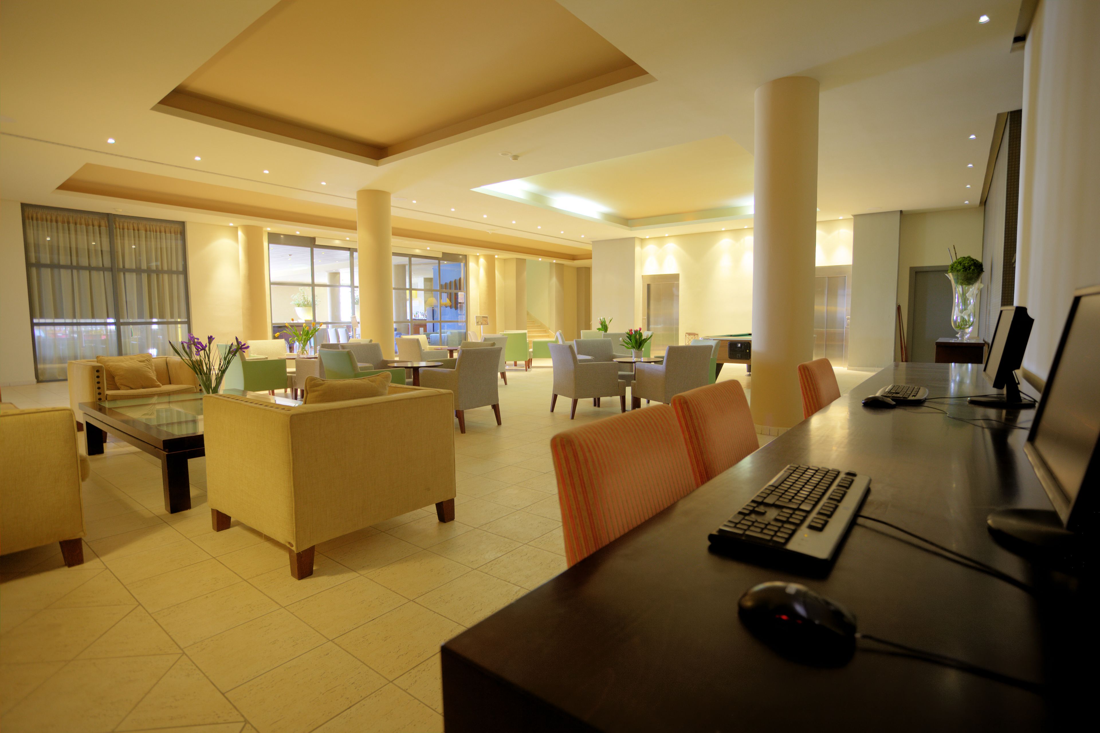 Un amplio vestíbulo de hotel con varias zonas de estar, una recepción y una computadora.