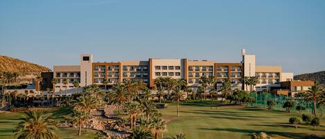 A hotel with multiple floors, a golf course, and palm trees.