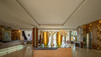 A spacious lobby with a reception desk, large golden vases, and a staircase leading to upper floors.
