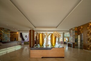 A spacious lobby with a reception desk, large golden vases, and a staircase leading to upper floors.