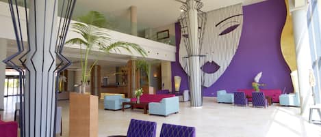 Un vestíbulo amplio con diseño moderno, que cuenta con un mostrador de recepción, zona de estar y una gran obra de arte abstracta en la pared.