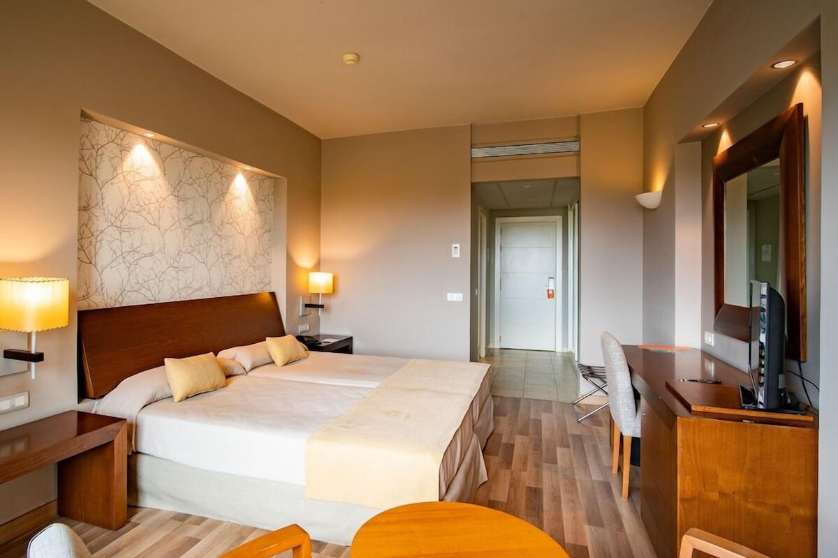 Una habitación de hotel con una cama grande, mesitas de noche, un escritorio, una silla y una televisión.
