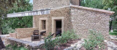 A stone building with a covered patio area, two doors, and outdoor seating.