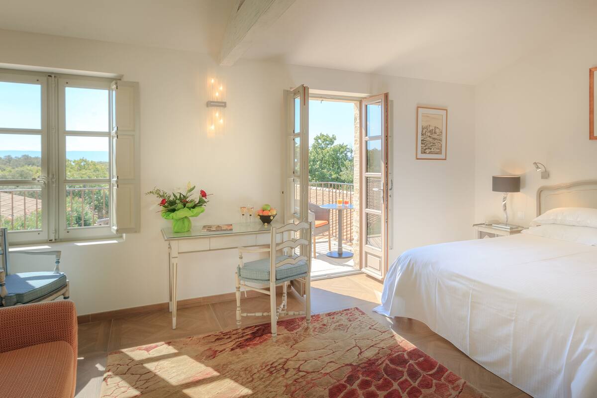 A bedroom with a bed, a desk with a chair, a balcony, and a view of the outdoors.