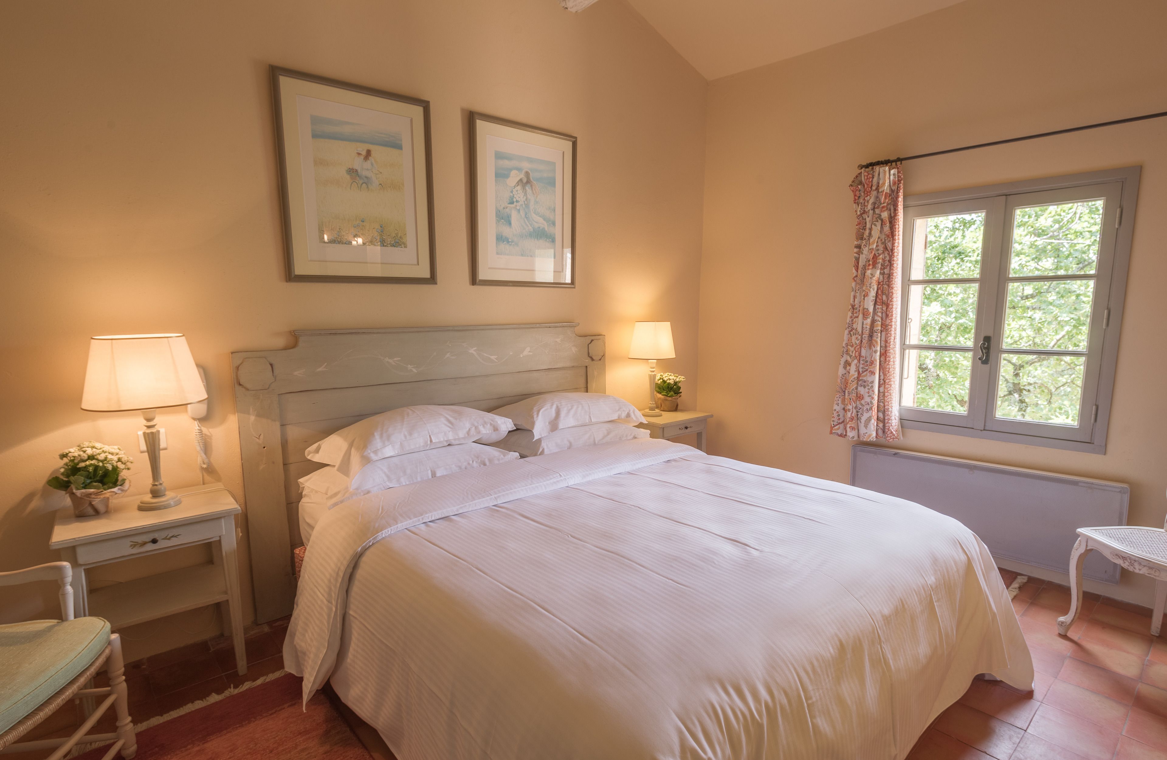 A bedroom with a large bed, two bedside tables with lamps, a chair, and two framed pictures on the wall.