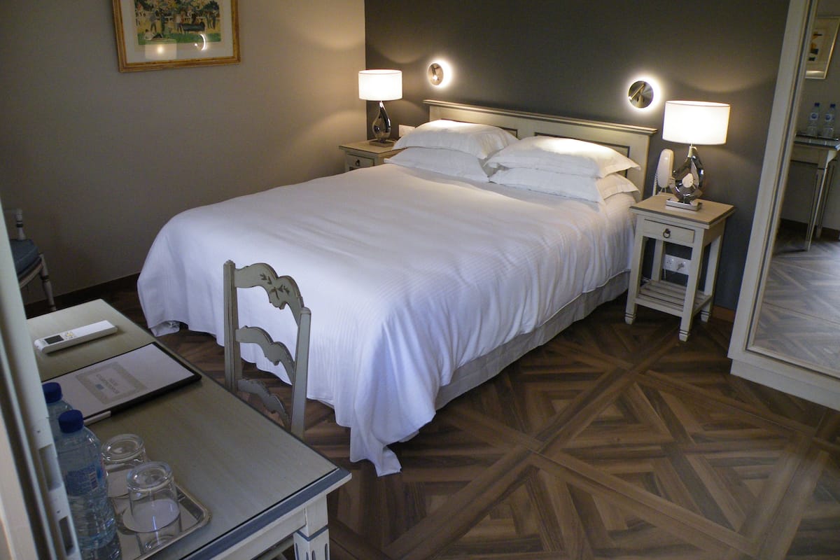 A hotel room with a large bed, two bedside tables with lamps, a desk with a chair, and a mirror.