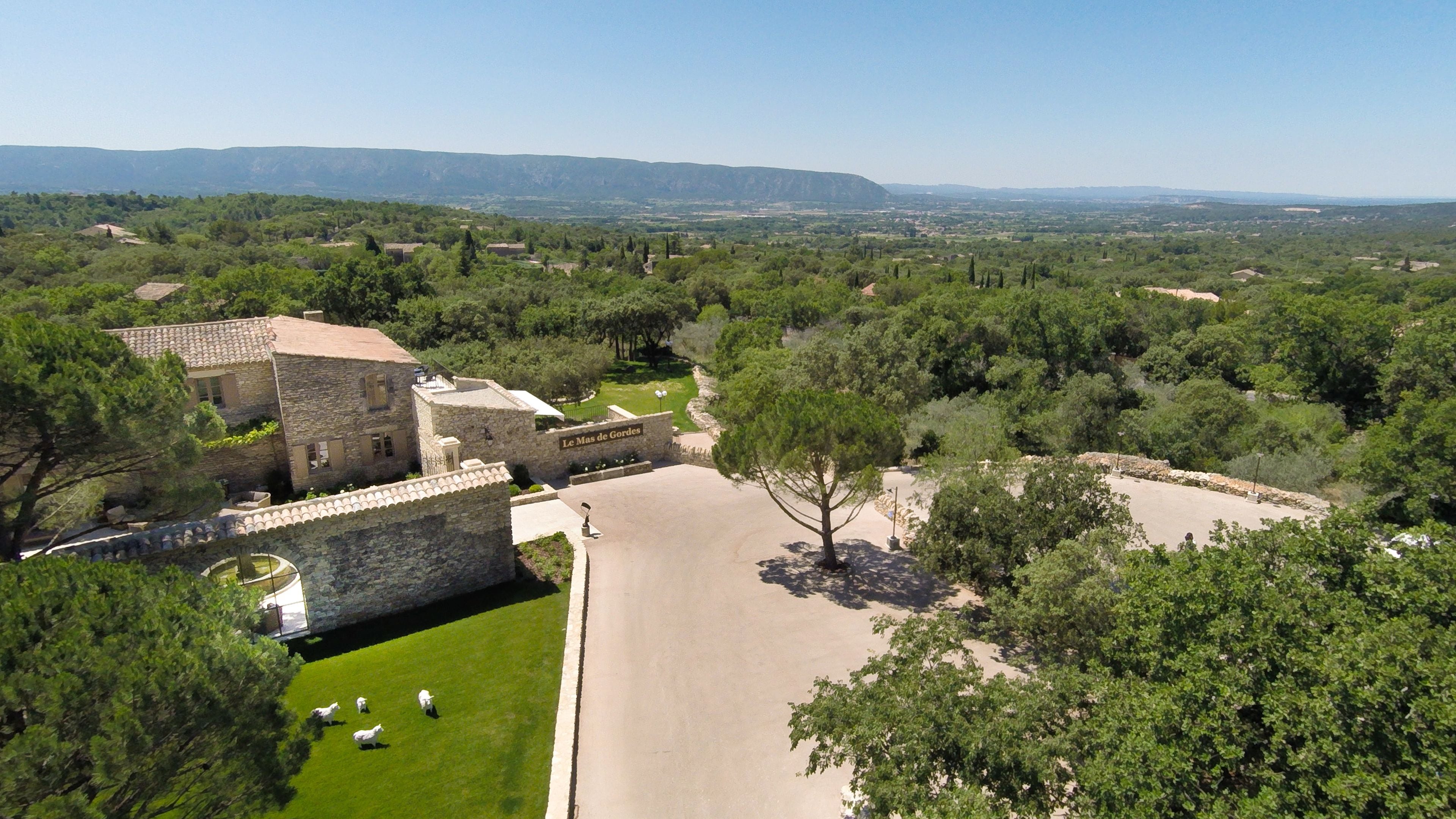 A stone building with a courtyard, surrounded by trees and a view of distant hills.