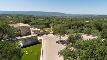 A stone building with a courtyard, surrounded by trees and a view of distant hills.