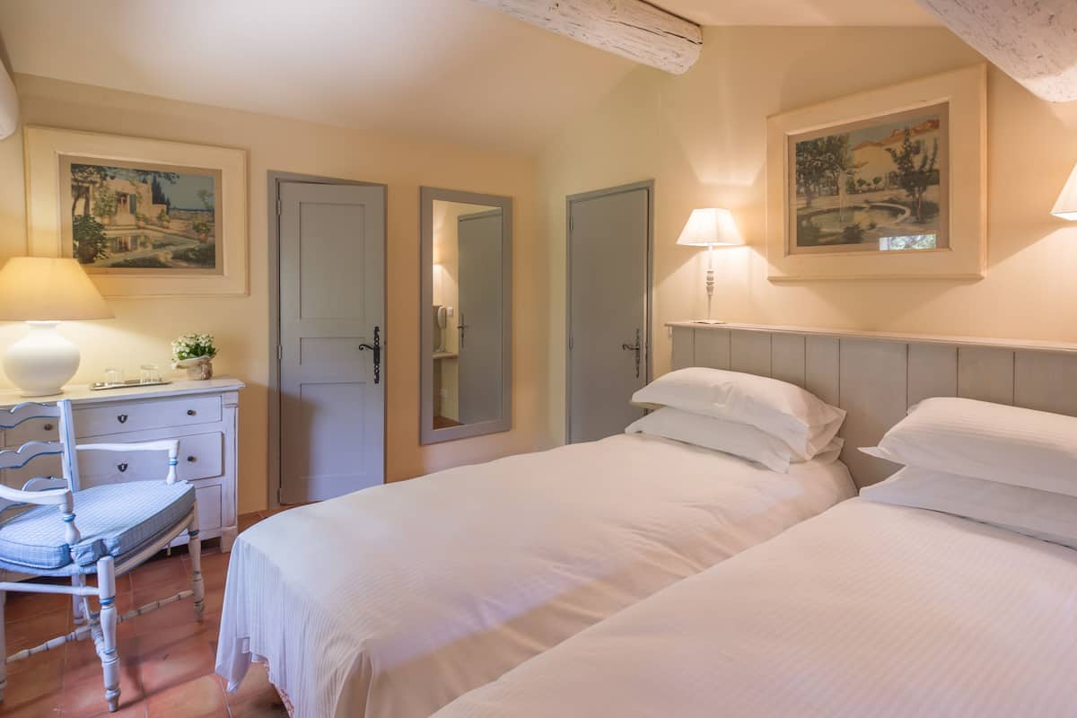 A bedroom with two beds, a dresser, a chair, and two wall-mounted lamps.