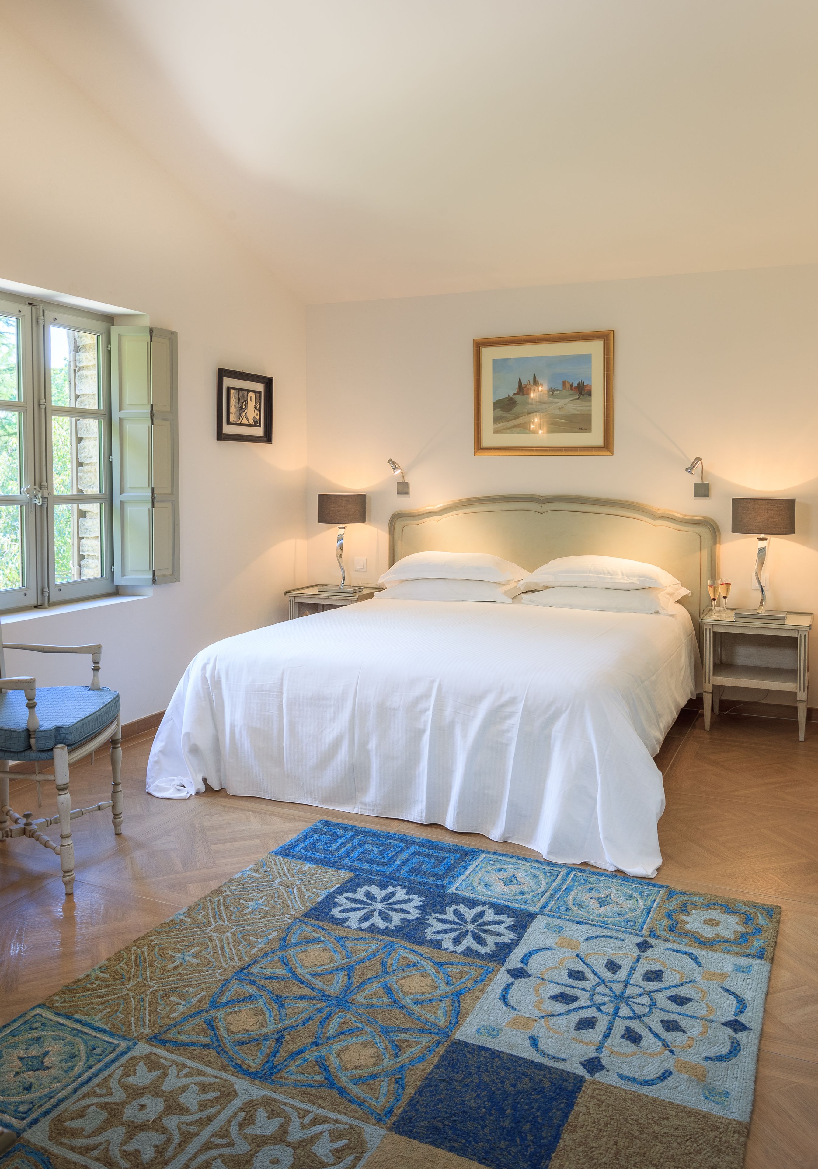 Une chambre à coucher comprenant un lit, deux tables de chevet, une chaise, une fenêtre avec des volets et un tapis à motifs.