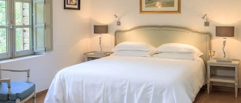 Une chambre à coucher comprenant un lit, deux tables de chevet, une chaise, une fenêtre avec des volets et un tapis à motifs.