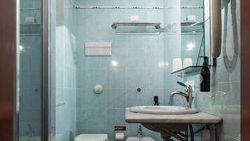 Un baño moderno con cabina de ducha de vidrio, inodoro blanco, bidé y lavamanos con espejo.