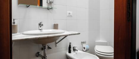 A modern bathroom with a wooden floor, a white sink, a bidet, and a toilet.