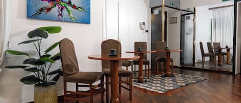 A modern hotel lobby with wooden flooring, a large abstract painting, a potted plant, and a mirror reflecting the room.
