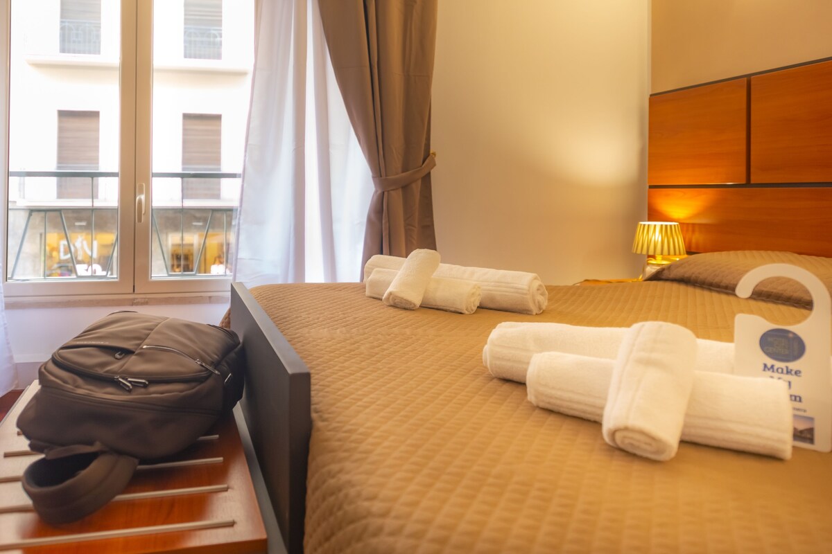 A hotel room with a bed, a suitcase, and a window with curtains.