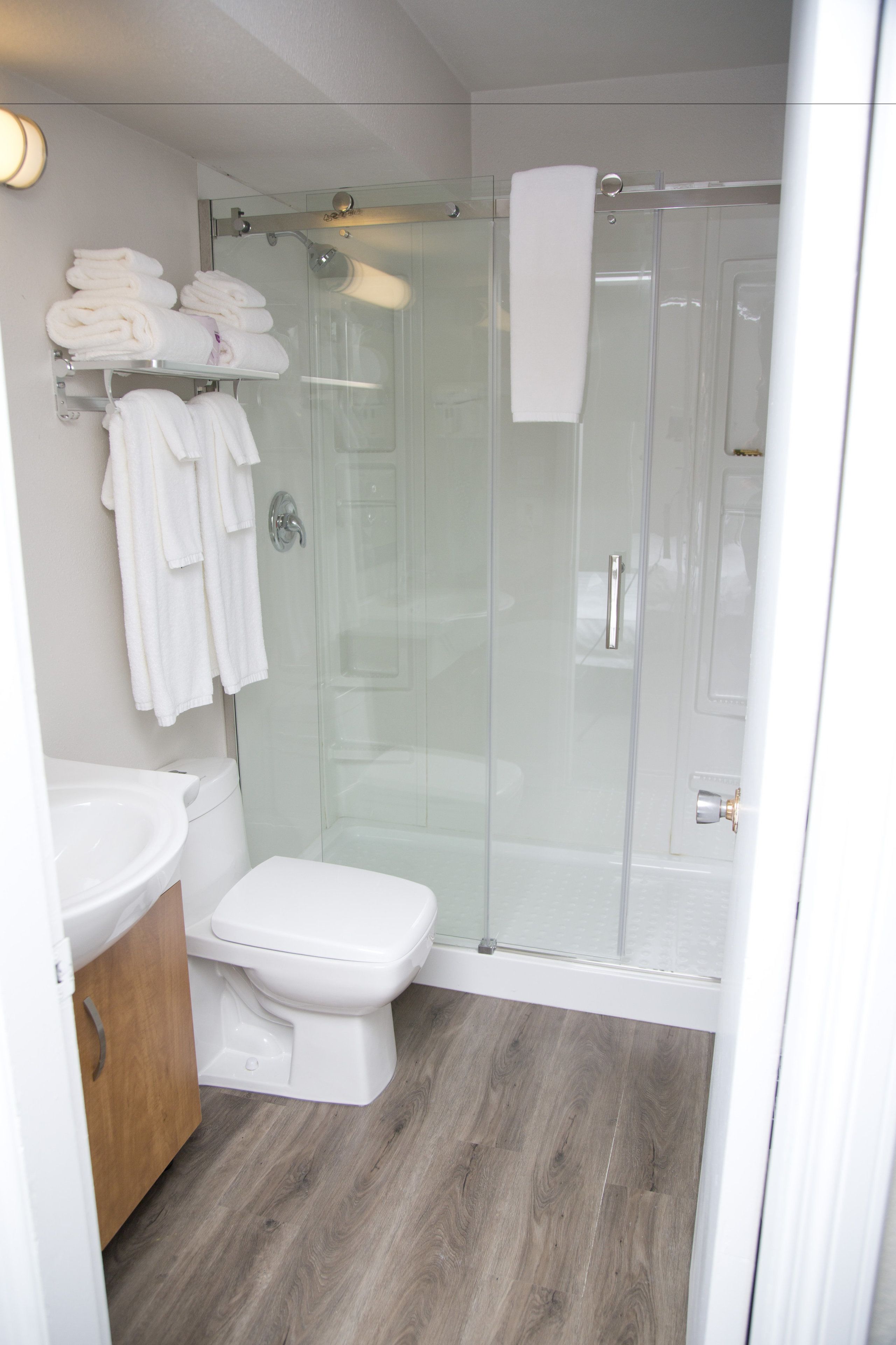 A modern bathroom with a glass-enclosed shower, a white toilet, and a sink with a wooden cabinet.