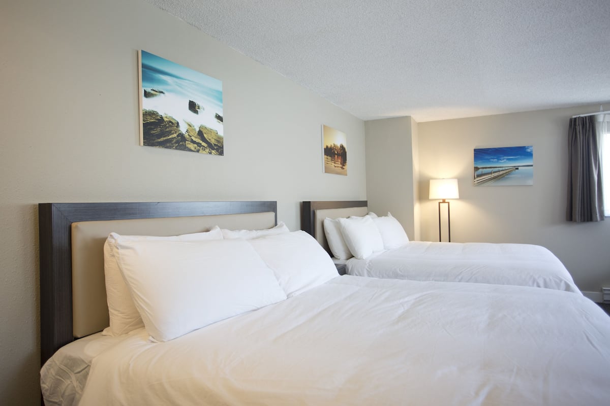 A hotel room with two beds, a nightstand, and wall art.