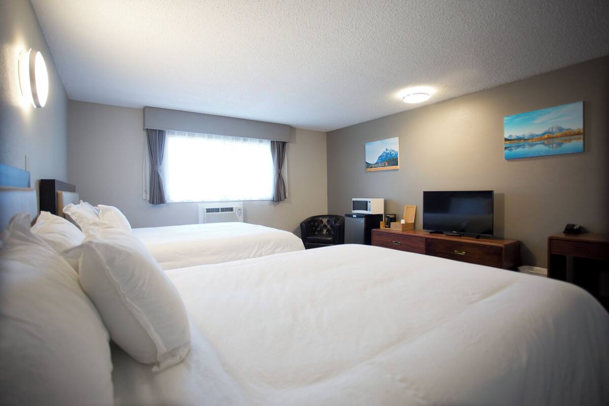 A hotel room with two beds, a TV, a desk, and a painting on the wall.