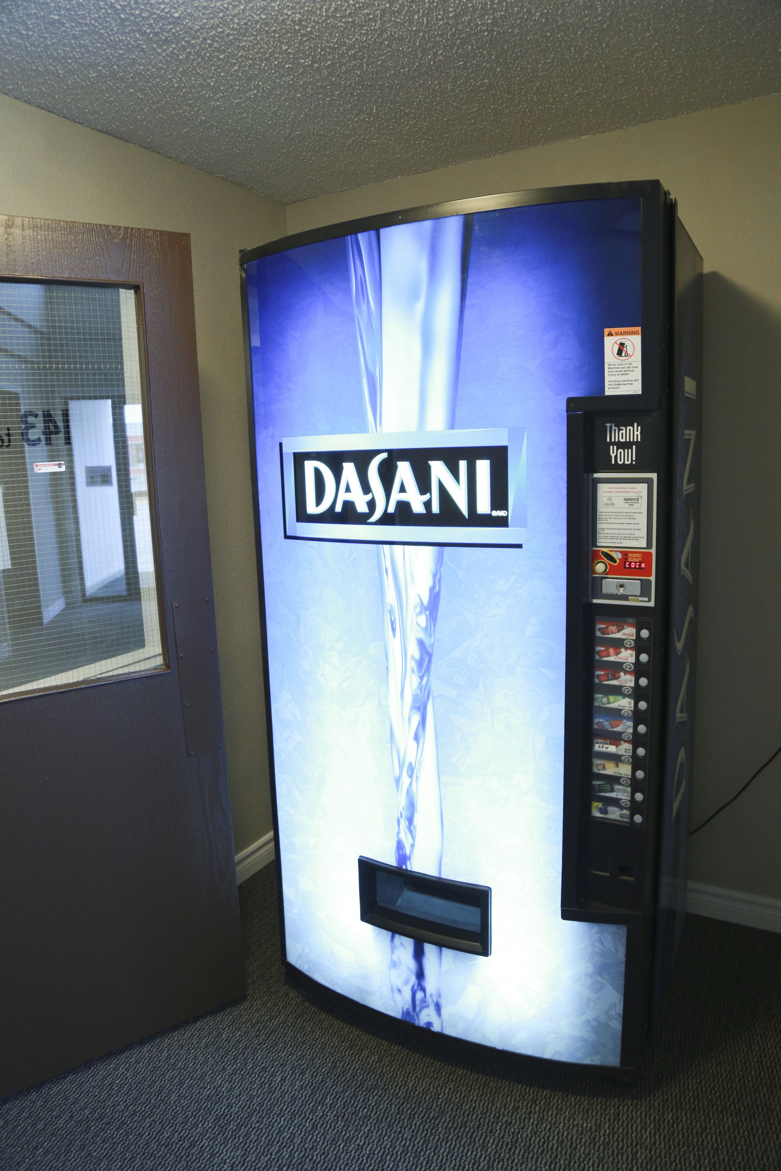 Un dispensador de agua Dasani con diseño azul y una etiqueta de advertencia en el lado derecho.