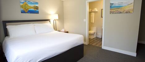 A hotel room with a large bed, a nightstand, a lamp, and two paintings on the walls.