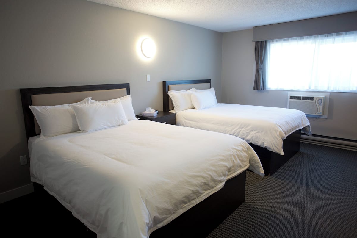 Two single beds with headboards, a bedside table with a lamp, a window with curtains, and an air conditioning unit.