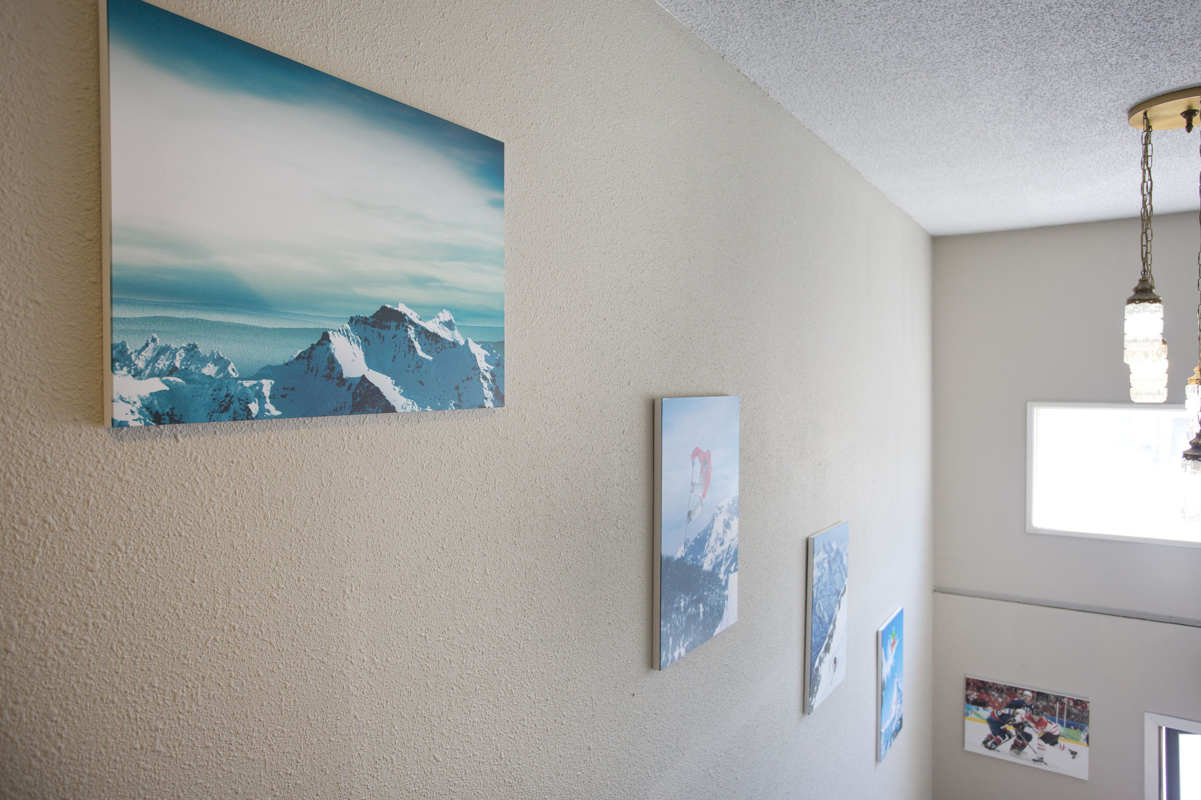 A room with a large mountain painting on the wall, a ceiling light, and a window.
