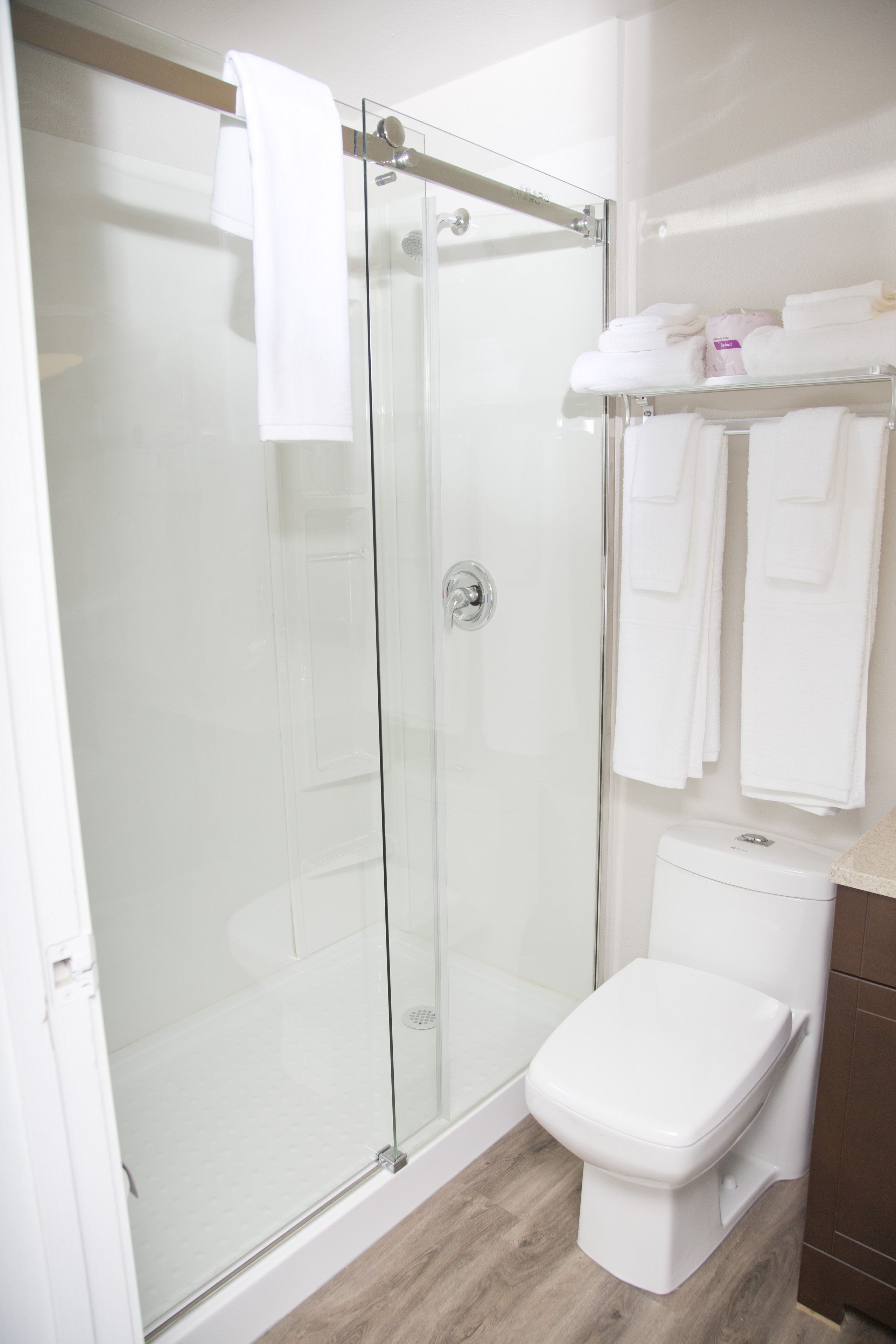 A modern bathroom with a glass shower enclosure, a white toilet, and a towel rack with neatly folded towels.