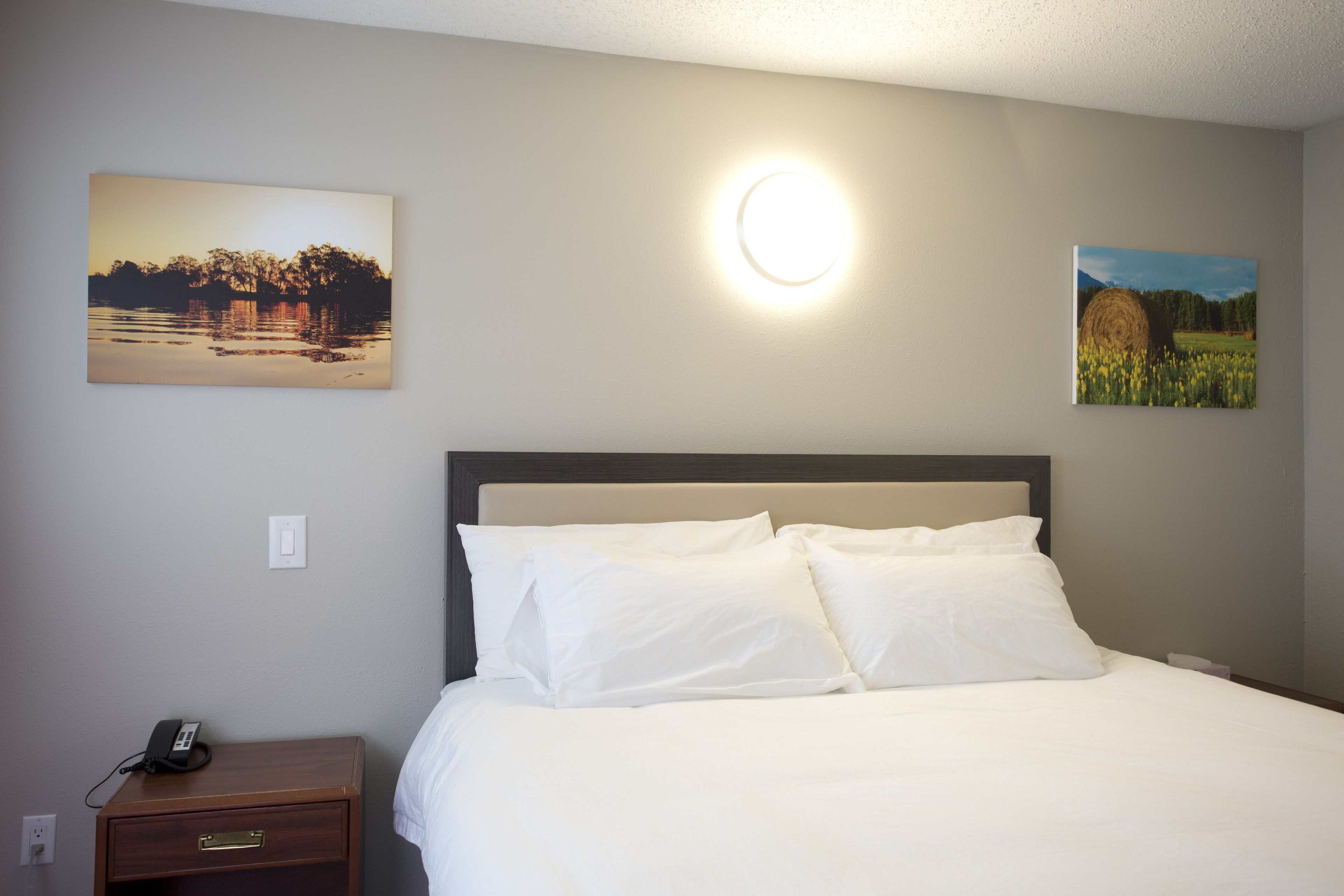 Una habitación de hotel con una cama, una mesita de noche con un teléfono y dos cuadros colgados en la pared.
