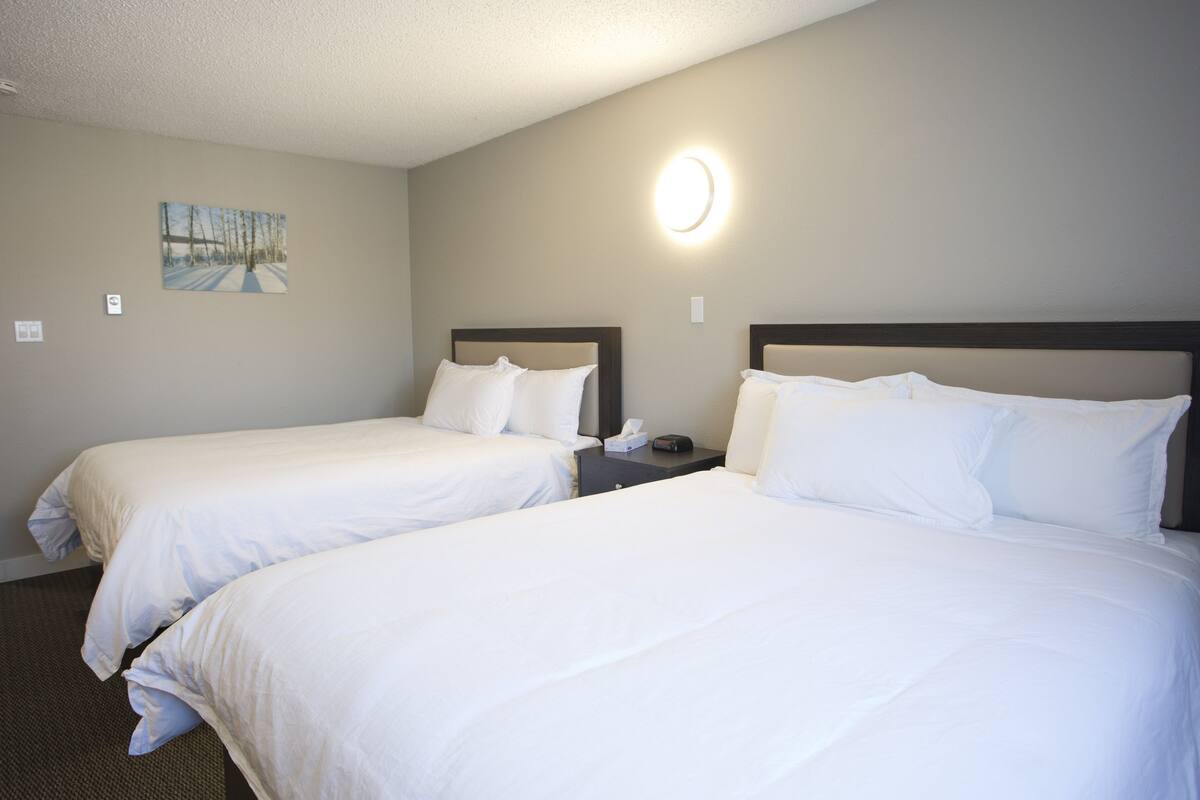 A hotel room with two beds, a nightstand, a wall-mounted light, and a painting.