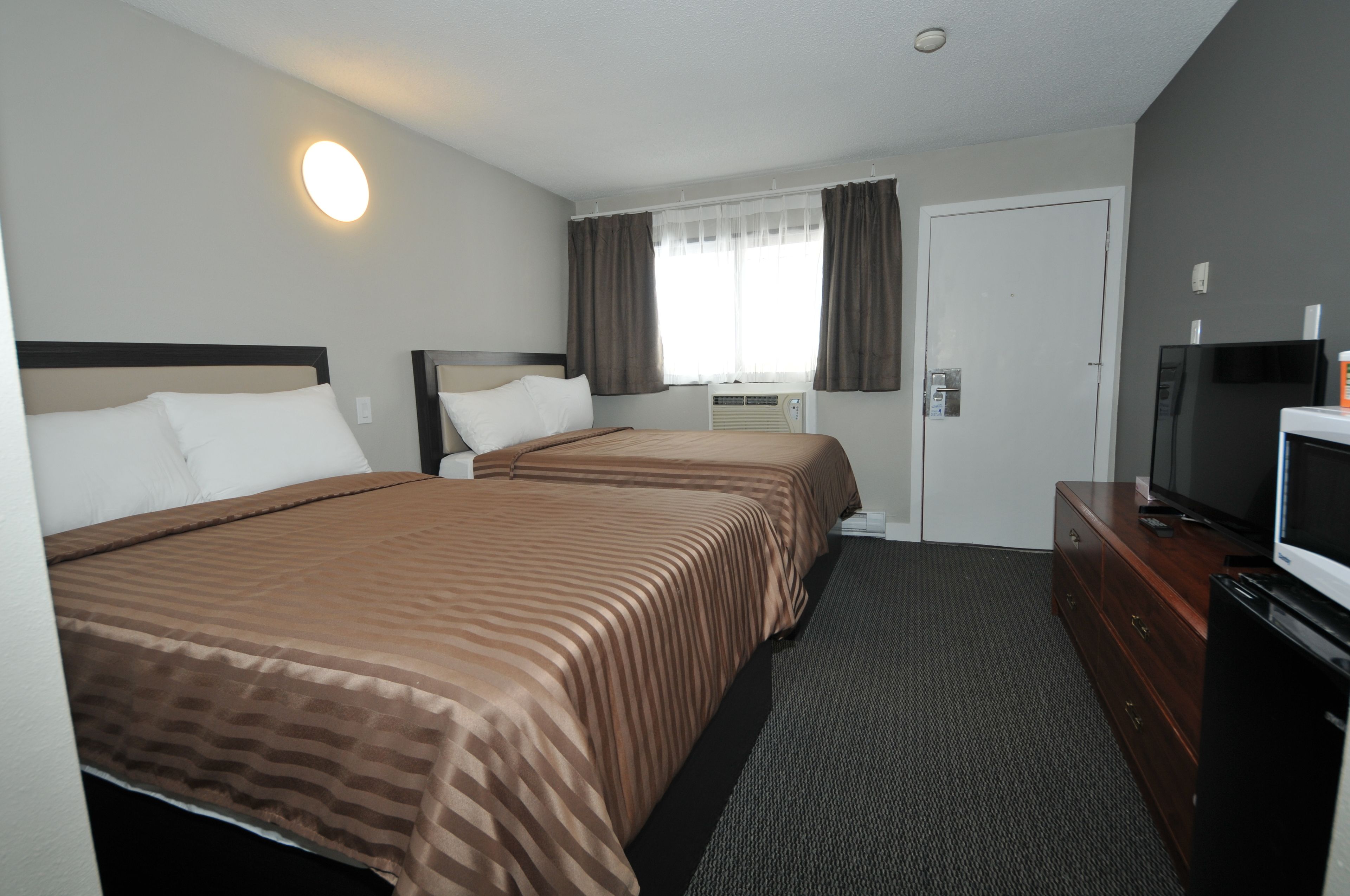 A hotel room with two beds, a television, a dresser, and an air conditioning unit.