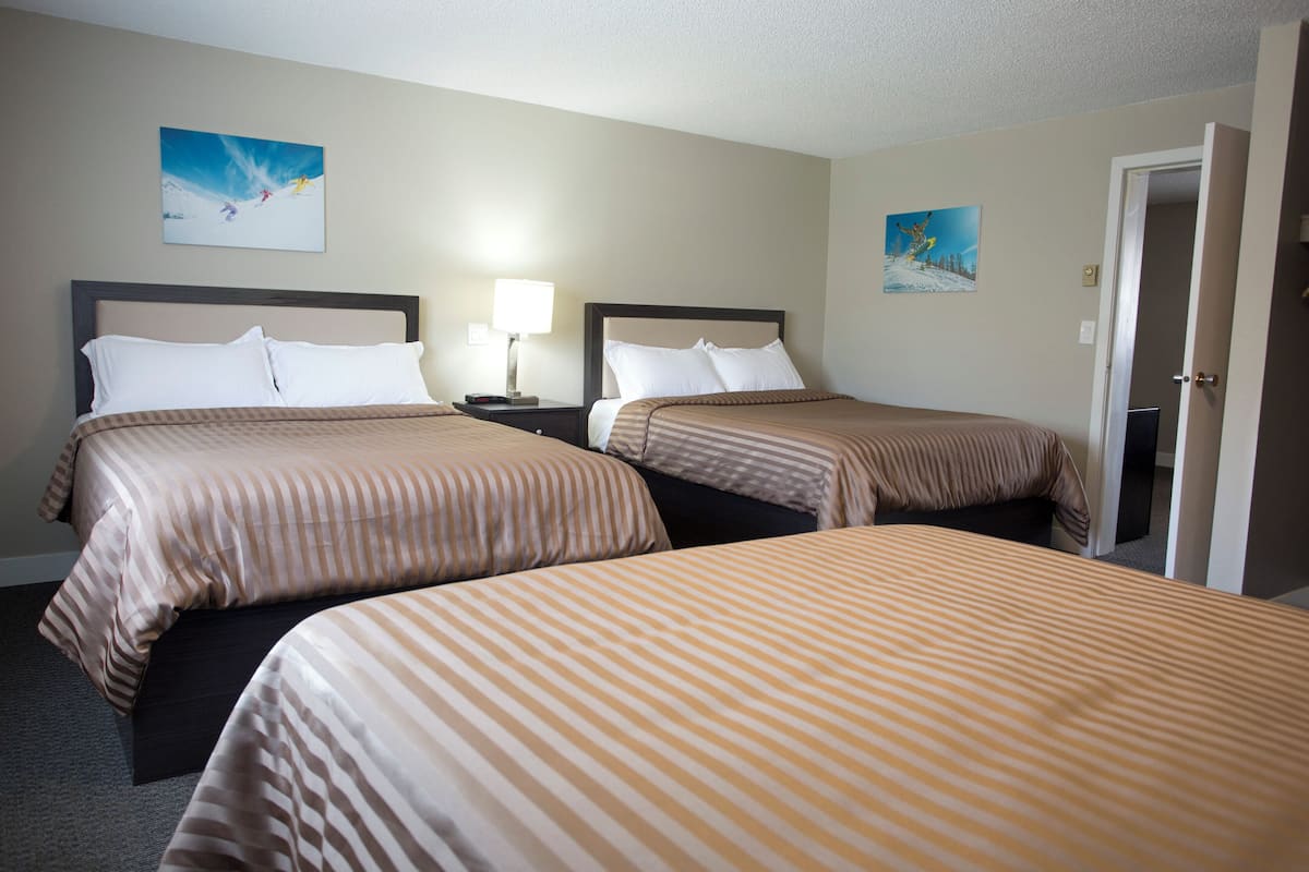 A hotel room with two beds, a nightstand with a lamp, and two wall-mounted paintings.