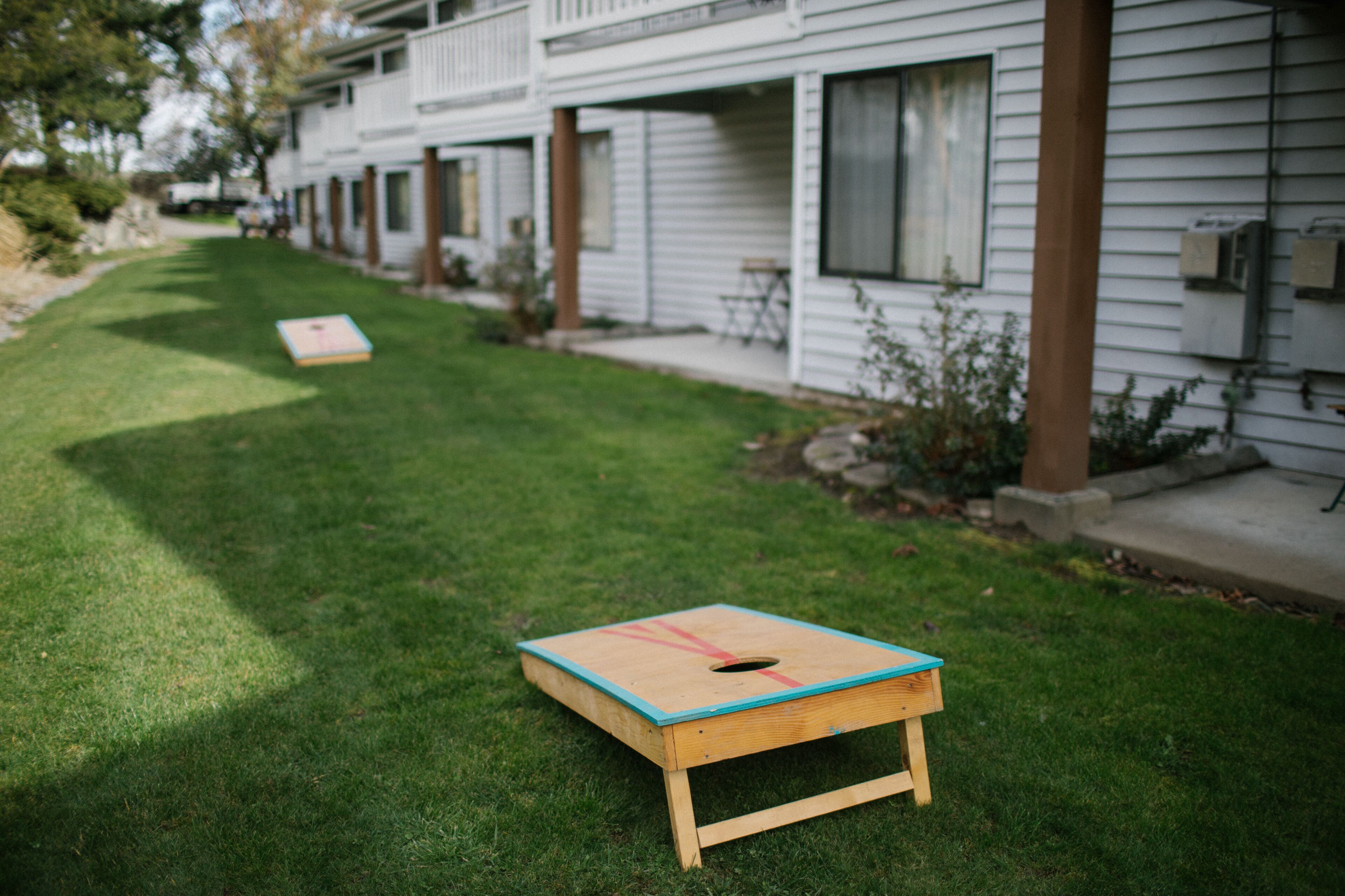 A row of white single-story houses with a grassy lawn and a wooden board game in the foreground.