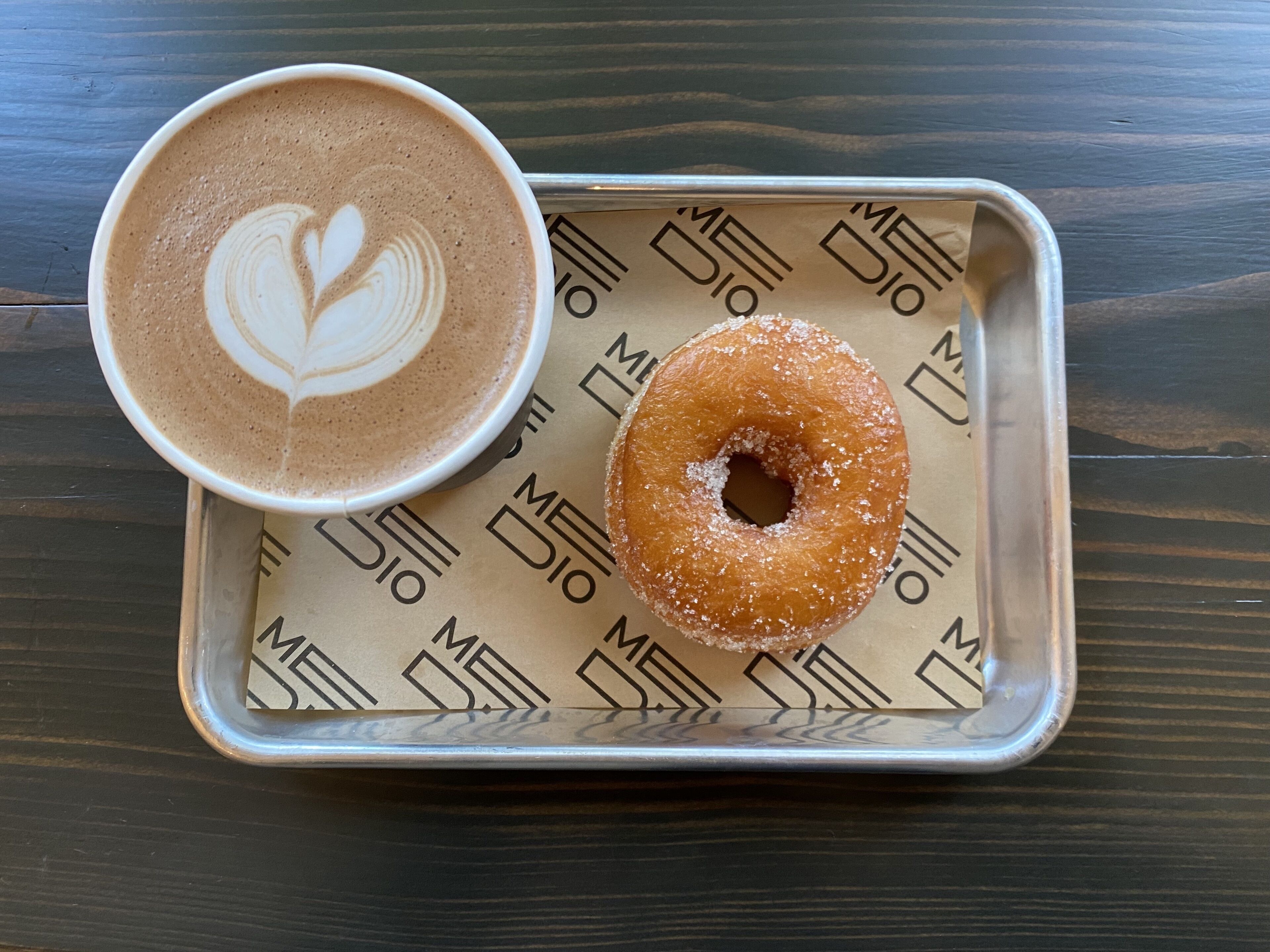 A tray with a cup of coffee and a sugar-coated donut on a wooden table.