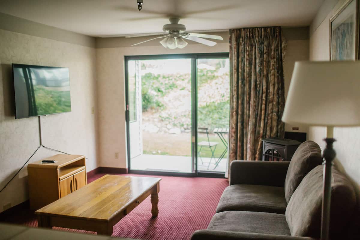 Una sala de estar con un sofá, una mesa de centro de madera, un televisor montado en la pared y un ventilador de techo.
