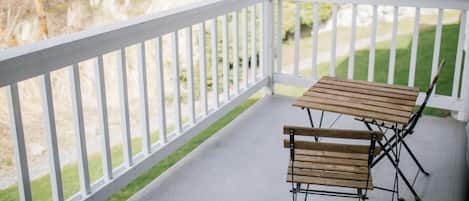 A covered outdoor area with a white railing, a wooden table, and two wooden chairs.