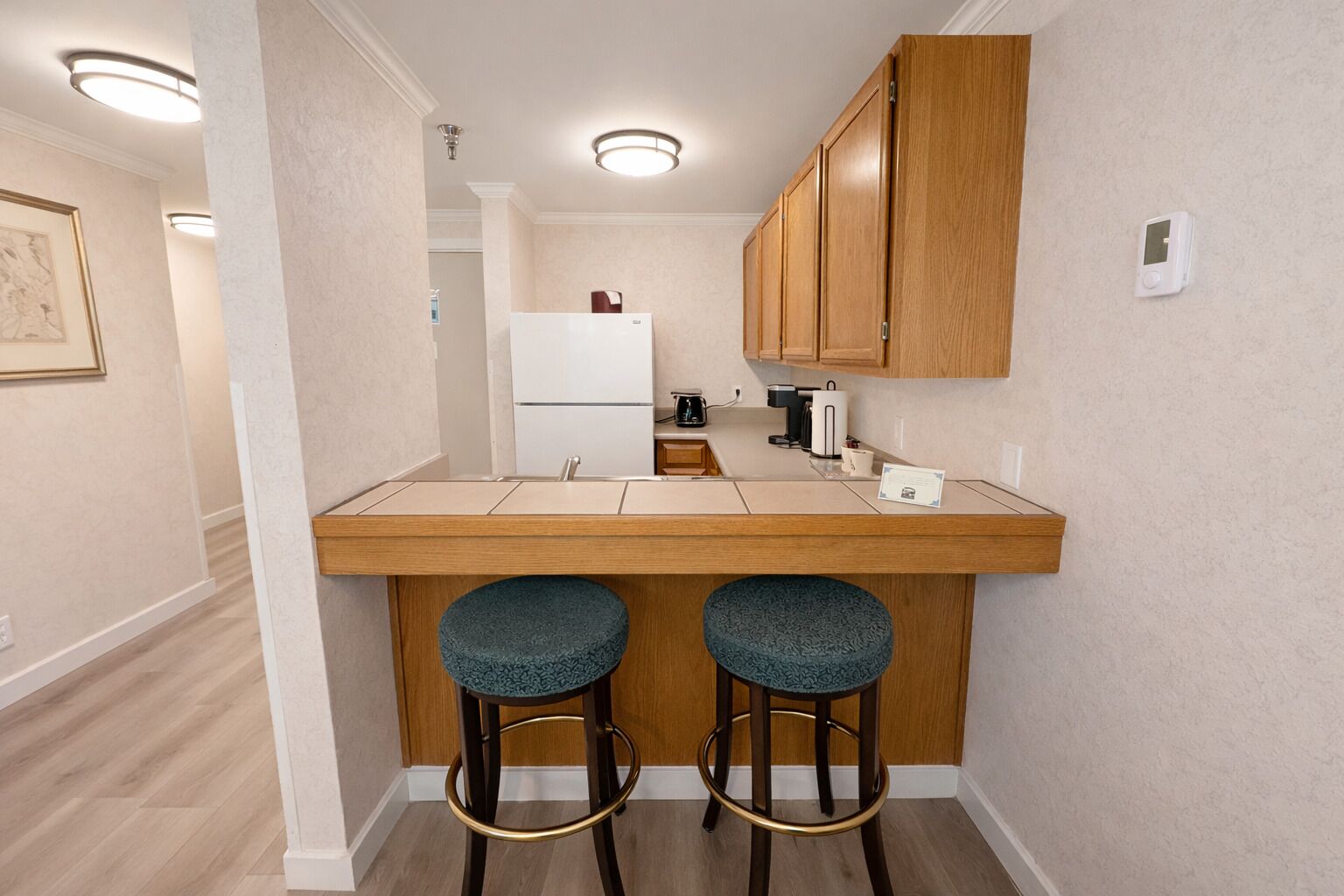 A kitchen with a wooden countertop, two bar stools, a refrigerator, and a coffee maker.