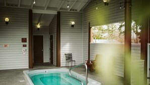 Zona de piscina exterior techada con un jacuzzi, bancos y señalización de salida de emergencia.