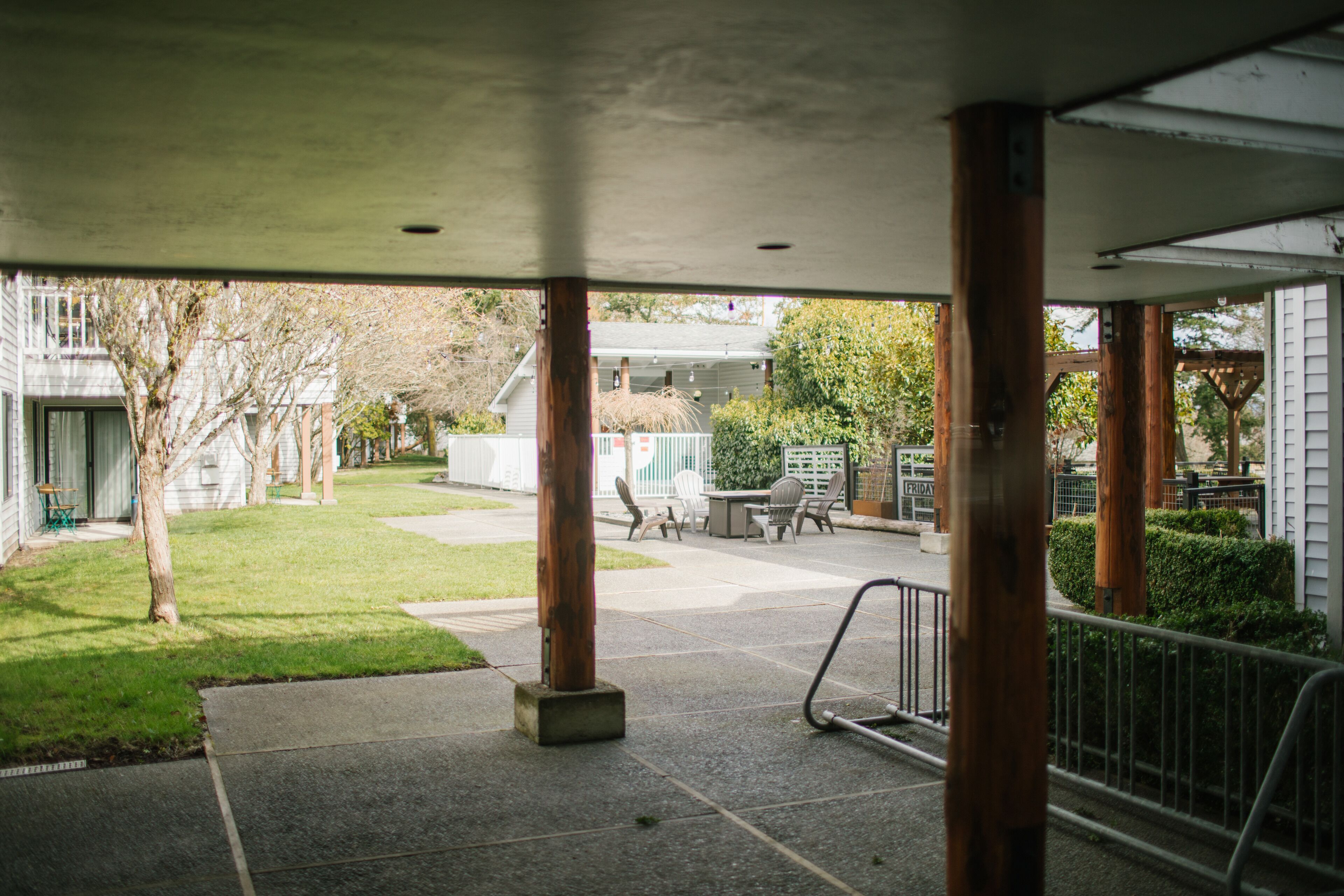 A covered outdoor area with a concrete floor, wooden pillars, and a metal railing.
