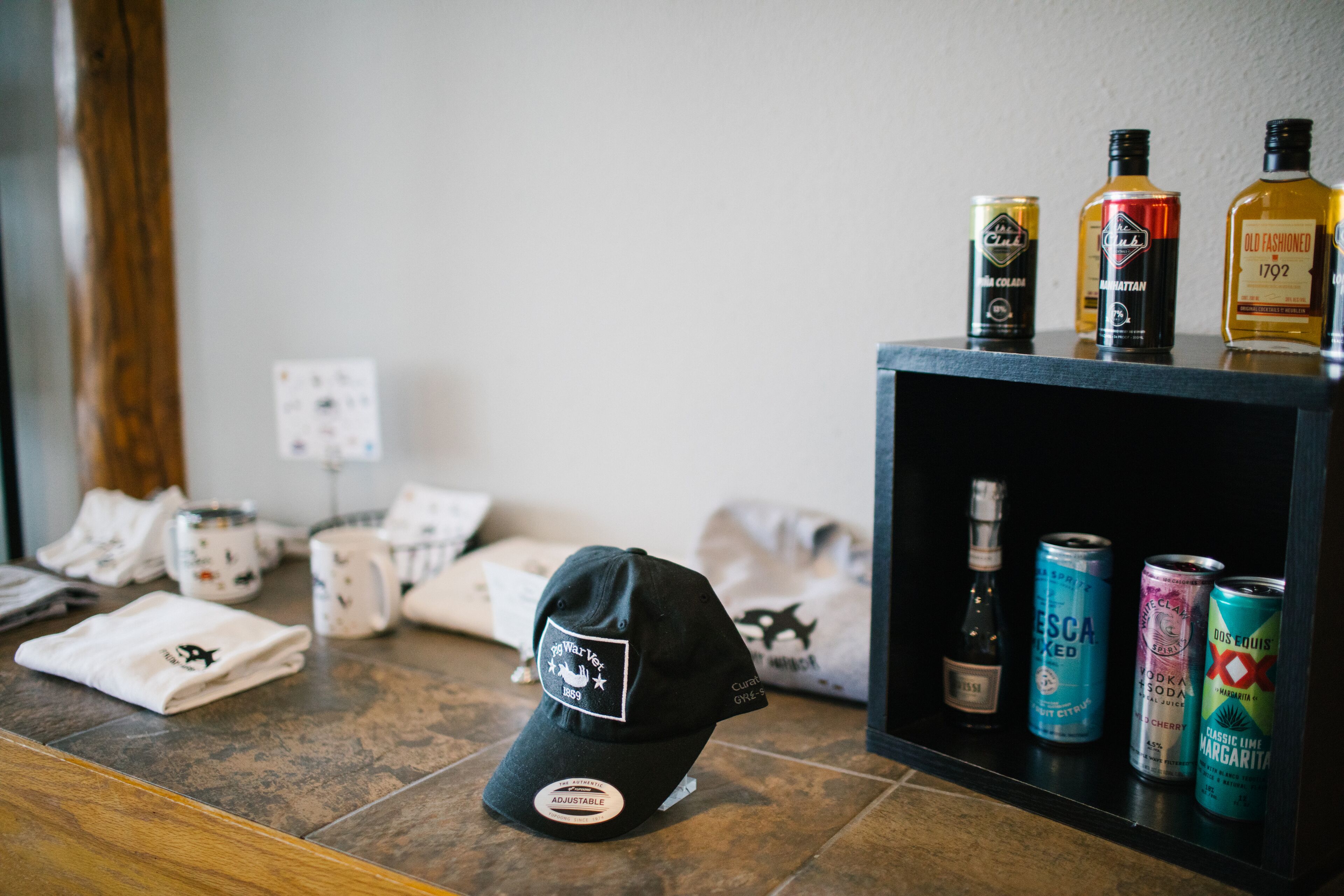 A black cap with a logo on a counter, surrounded by various beverages and cans.