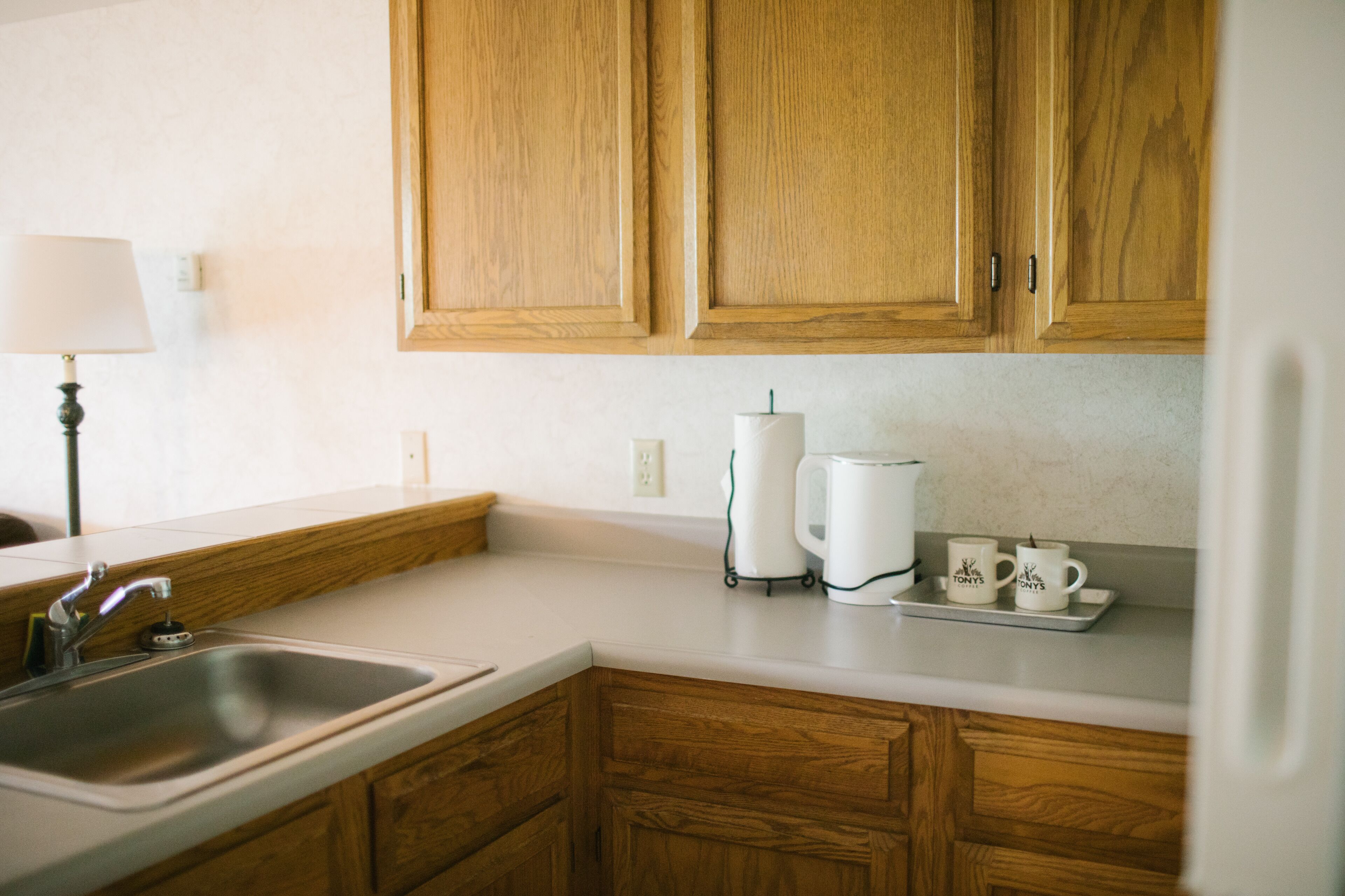 A kitchen with wooden cabinets, a sink, a coffee maker, and two mugs on the counter.