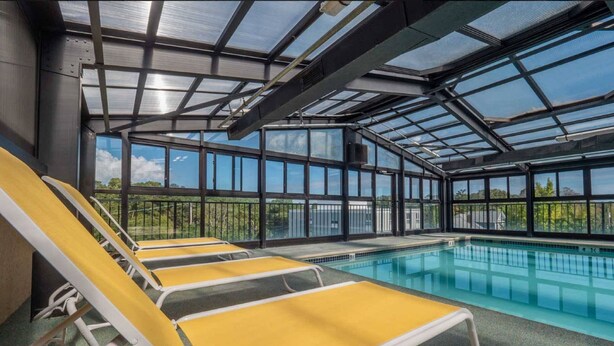 Zona de piscina con sillones amarillos y blancos, techo de cristal y vistas al exterior.