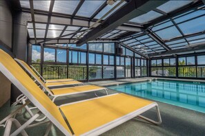 Zona de piscina con sillones amarillos y blancos, techo de cristal y vistas al exterior.