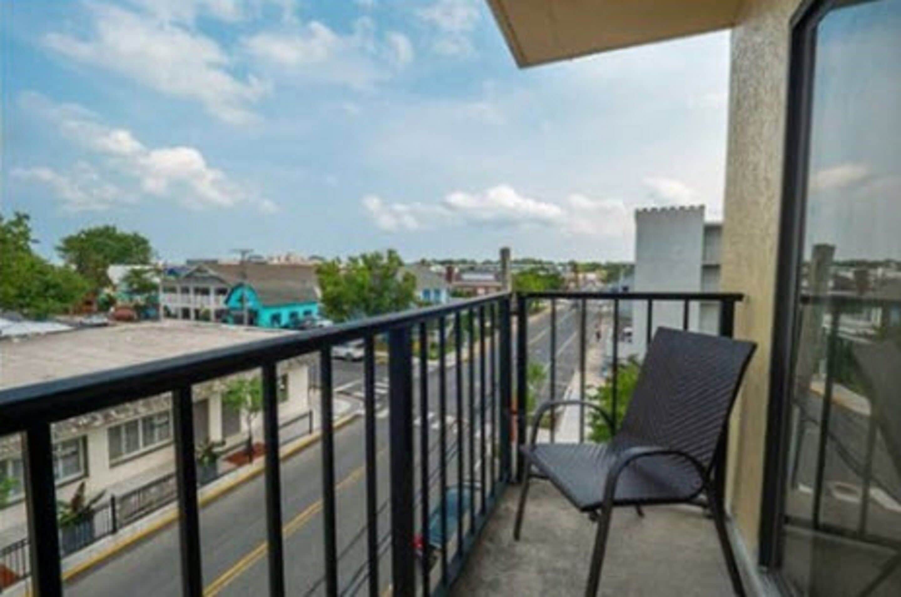 A balcony with a chair, a view of a street, and buildings in the background.