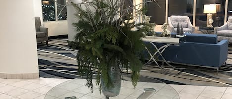 A modern lobby with a glass-top table, a potted plant, and a blue sofa.