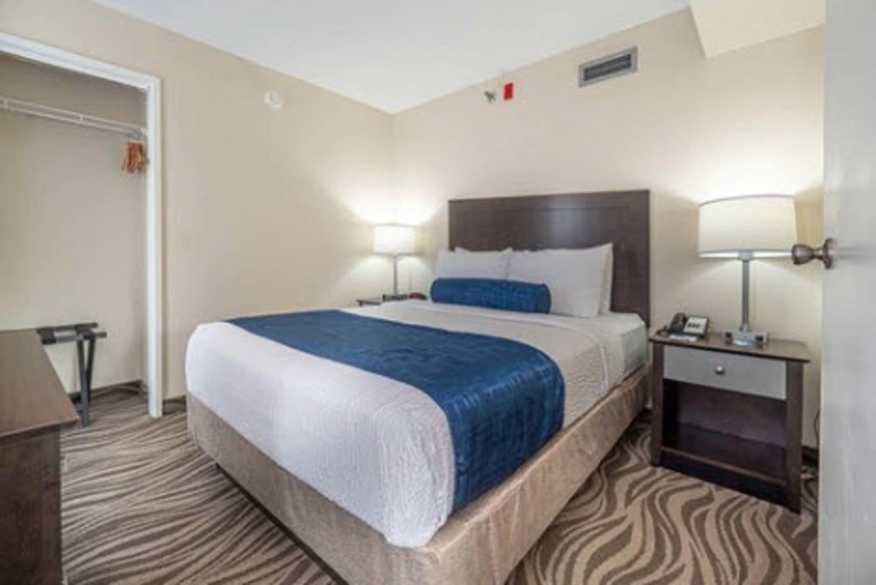 A hotel room with a large bed, two bedside tables with lamps, a wardrobe, and a carpeted floor.