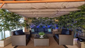 Un espacio exterior cubierto con sofás y una mesa de centro, rodeado de plantas en macetas y vistas al océano.