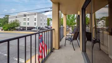 A hotel balcony with a view of a parking lot and a building across the street.