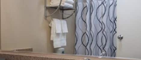 A bathroom with a granite countertop sink, a towel rack with folded towels, a shower curtain with a wavy pattern, and a mirror above the sink.